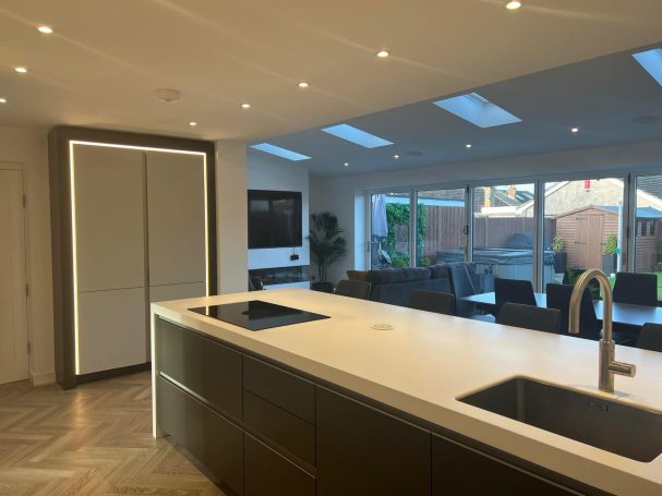 Modern kitchen with a large island, bright lights, and glass doors leading to a garden.
